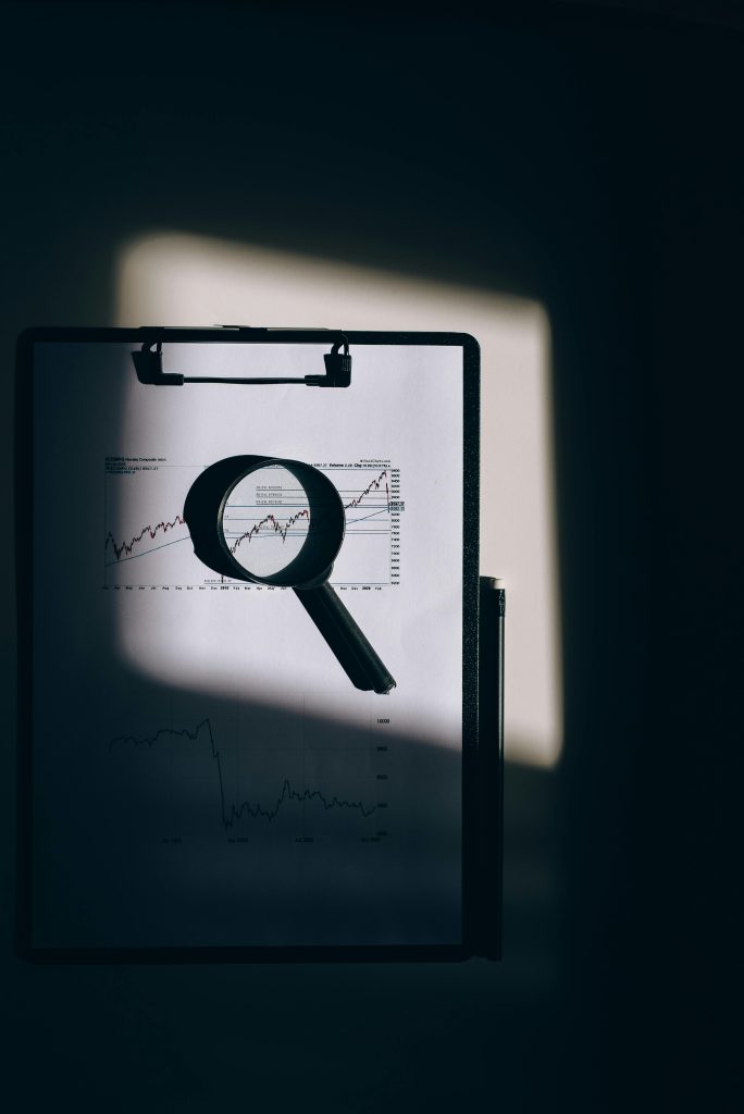 pexels-photo-5561921-5561921 A magnifying glass lays over a financial chart on a clipboard, casting intriguing shadows.